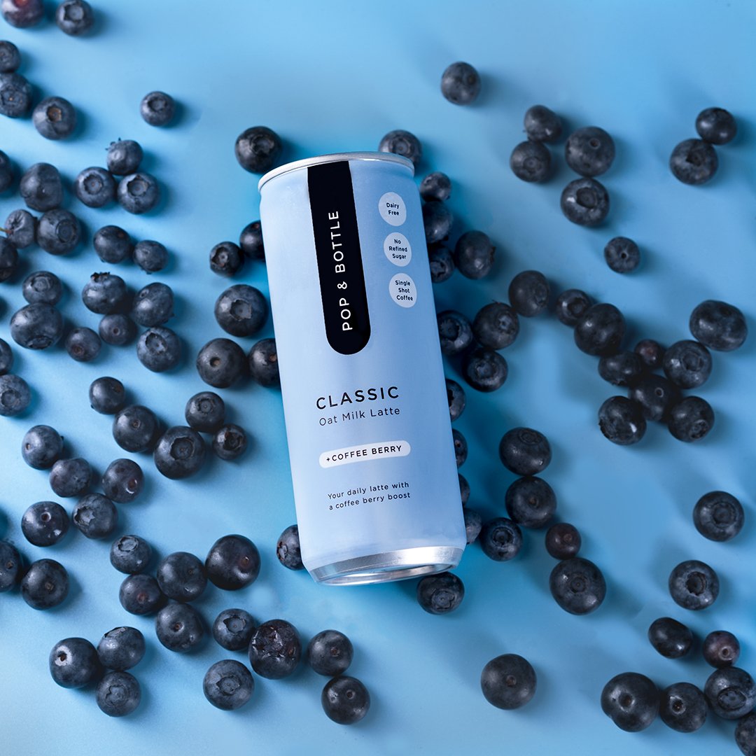 Clean product photography of a blueberry beverage can on a blue background with scattered blueberries