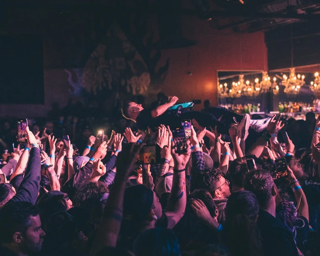 Crowd of people at a concert with one person crowd surfing above the audience while many take photos with their smartphones.