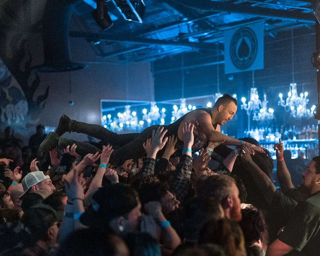 Musician crowd surfing at a concert with audience members holding him up.