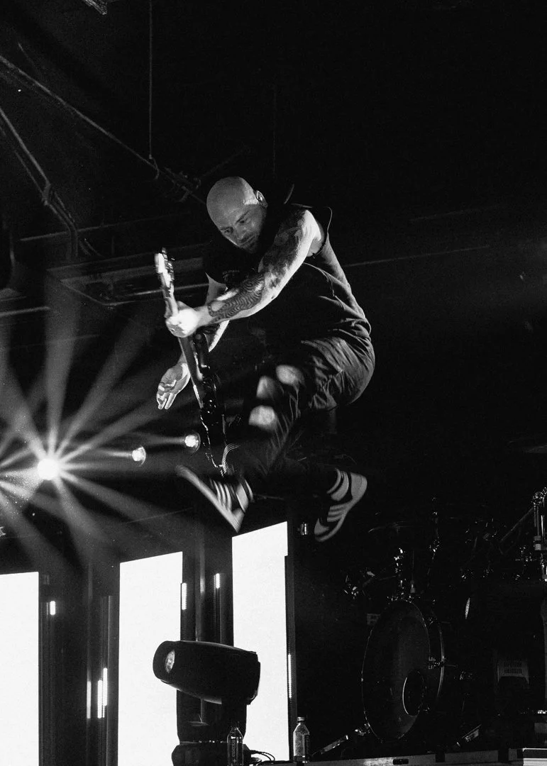A musician mid-air jumping with an electric guitar during a live concert.