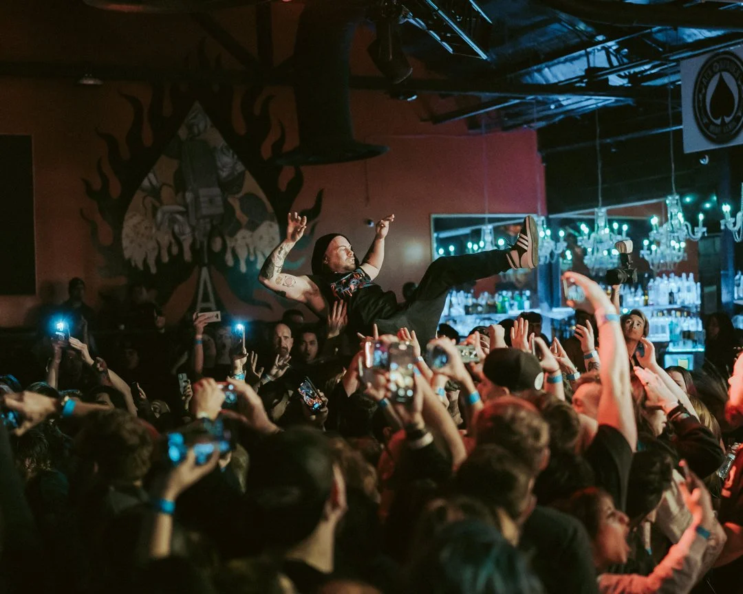 A man crowd surfing at a concert or music event, with audience members holding him up and taking photos.