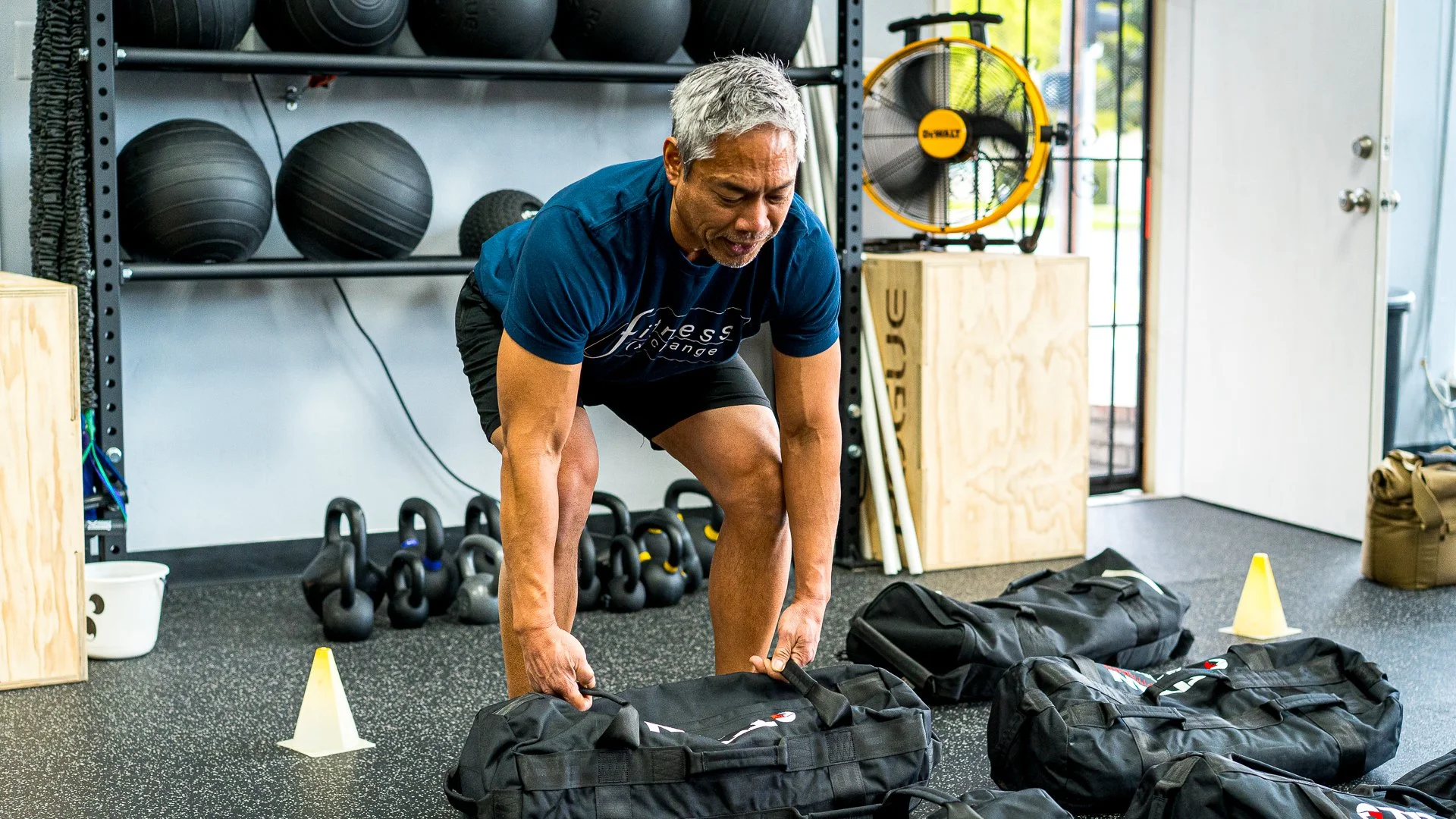 Man in a blue fitness shirt lifting a heavy bag