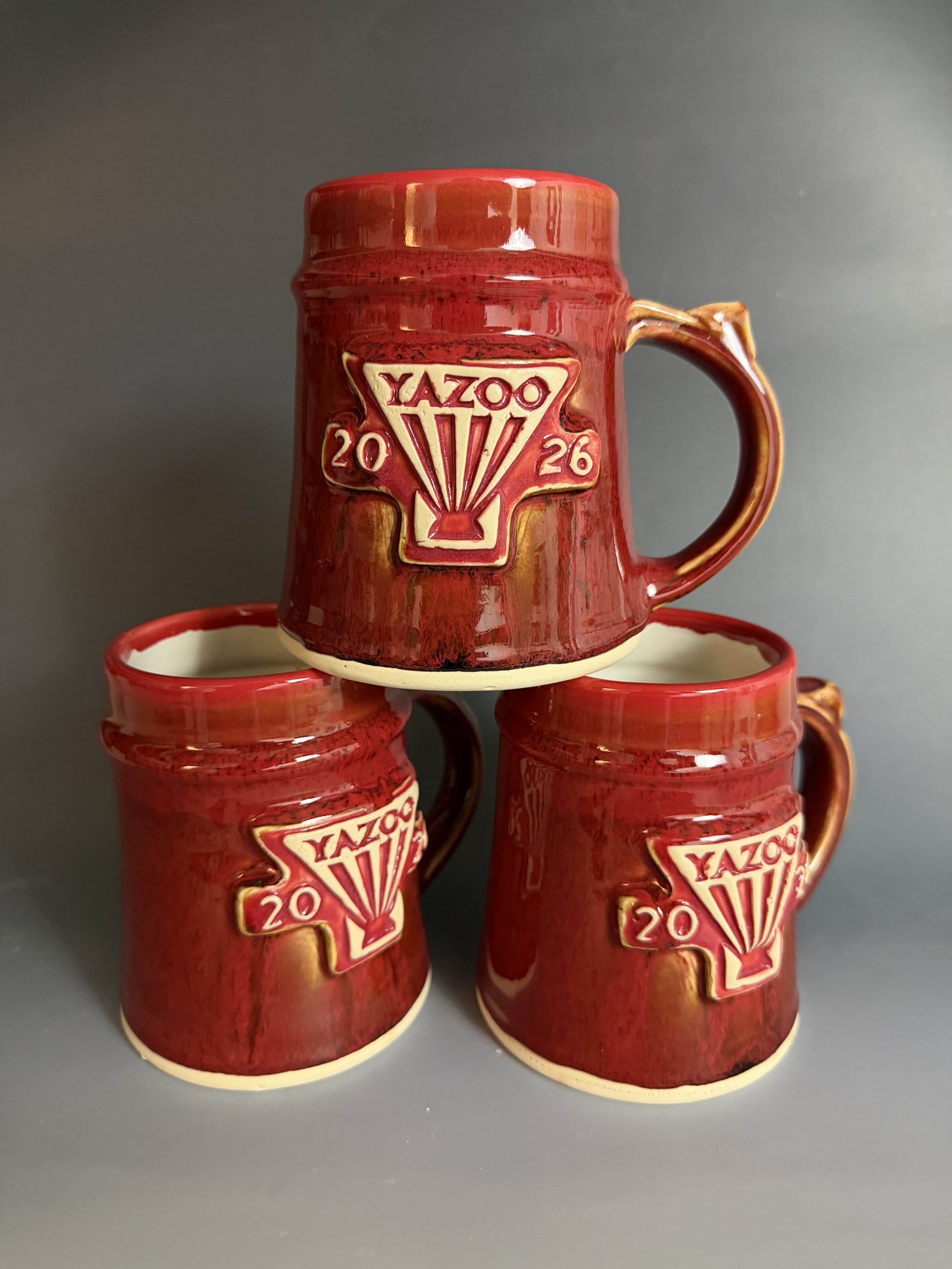 A stack of completed Yazoo 2026 Mug Club Mugs. Glazed with a custom red and tenmoku glaze. Made at Old School Farm Pottery, a nonprofit Nashville Pottery.