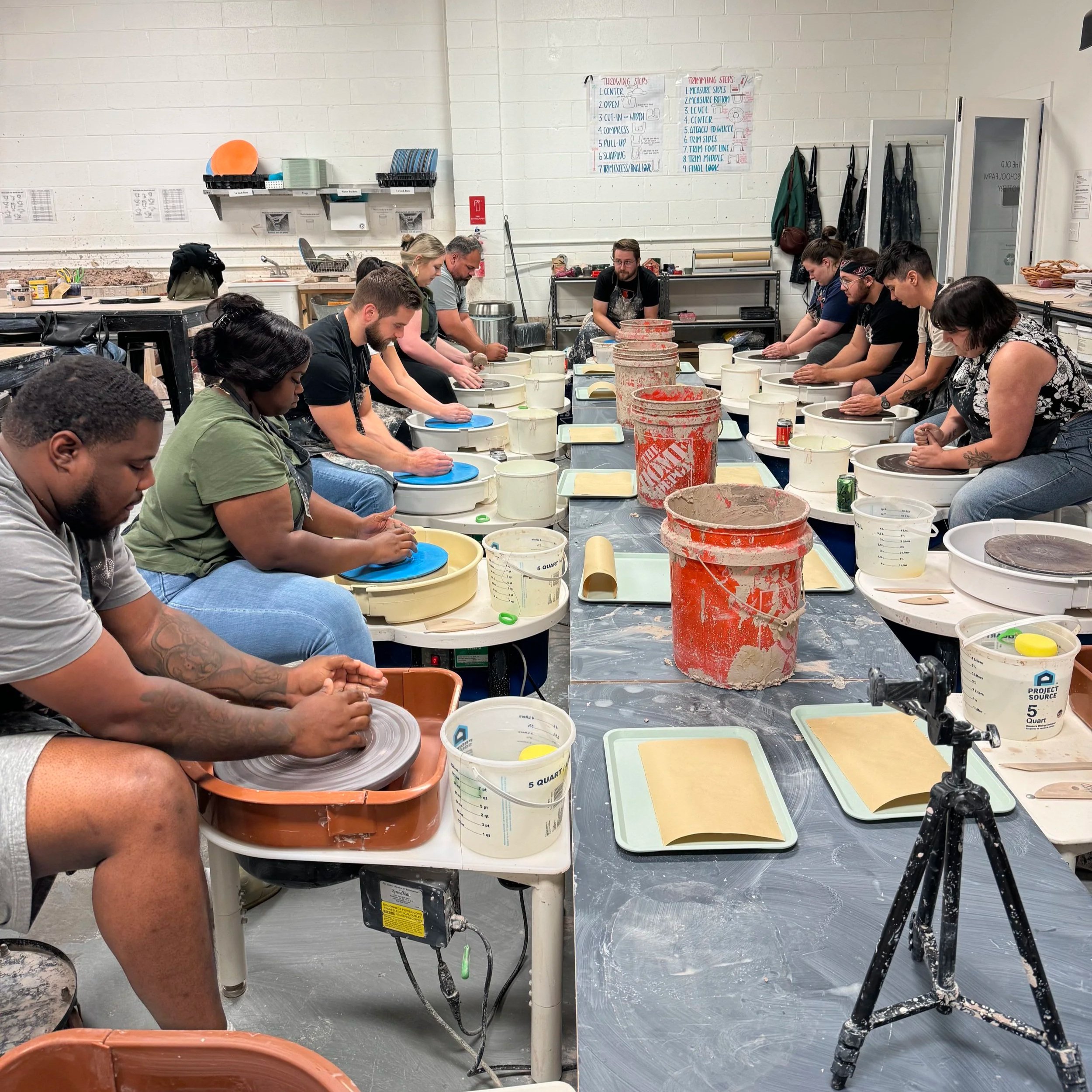 Two rows of people learning how to throw on a potter's wheel. A date night at Old School Farm Pottery, a nonprofit Nashville pottery
