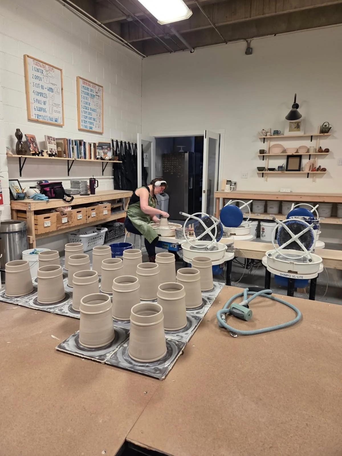 A group of thrown mug forms sitting on a table while the potter makes them in the background. Made at Old School Farm Pottery, a nonprofit Nashville Pottery.