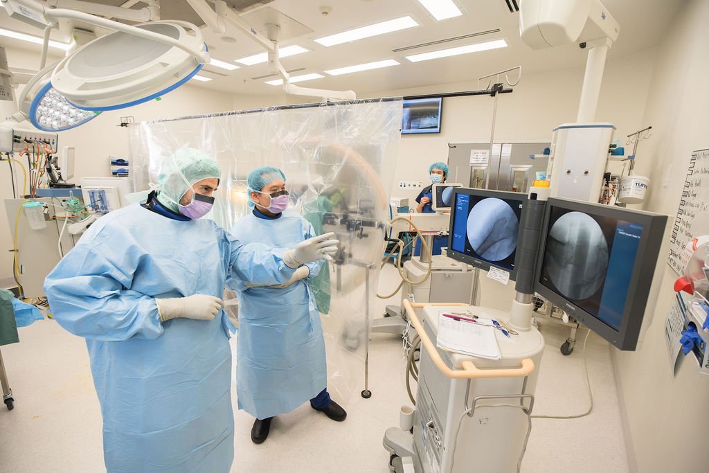Two surgeons in surgical gowns, masks, and gloves review live fluoroscopy images on dual monitors inside an operating theatre at Box Hill Hospital