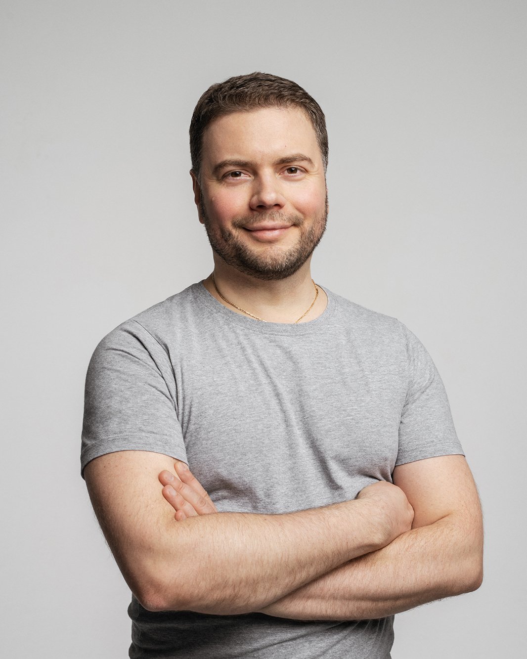A person wearing a gray t-shirt with arms crossed, smiling, in front of a plain white background.