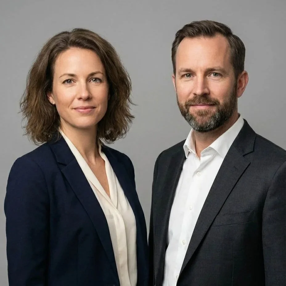A professional woman and man in business attire standing side by side against a gray background.