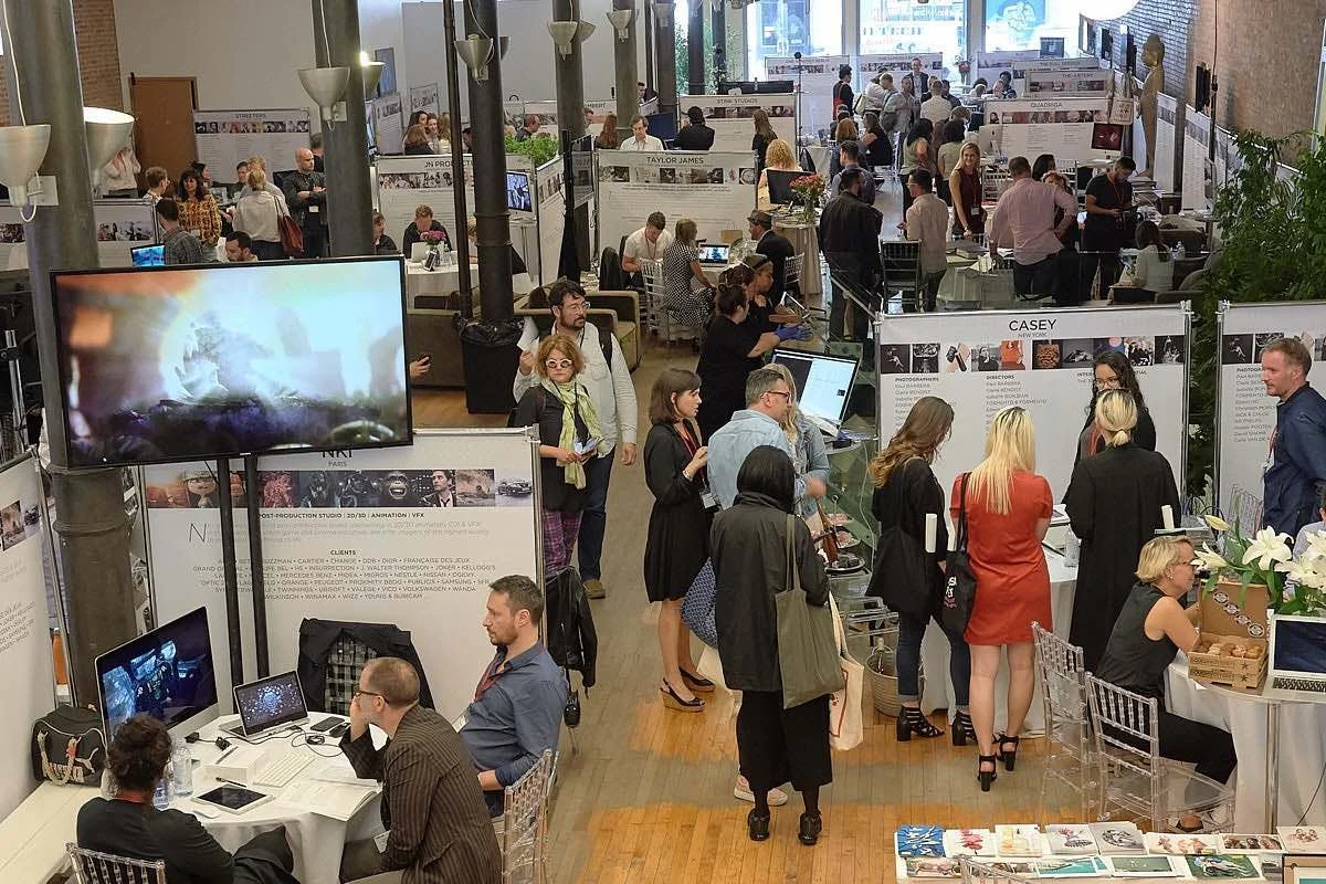 An indoor conference or exhibition with numerous booths, displays, and attendees engaged in discussions and viewing presentations.