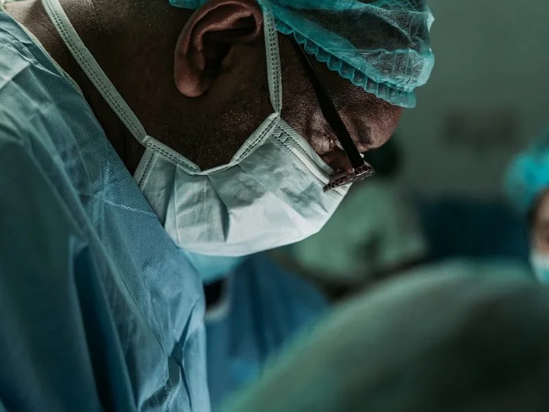 Close-up of a surgeon wearing a surgical mask, cap, glasses, and scrubs during an operation.