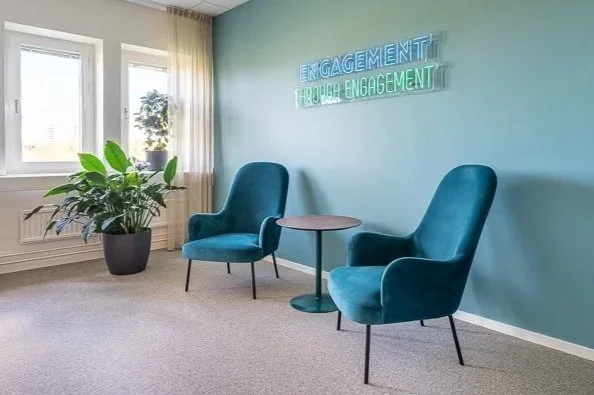 Informell mötesplats på Viatels kontor i Stockholm med fåtöljer, växtlighet och neonskylt som speglar företagets värderingar.