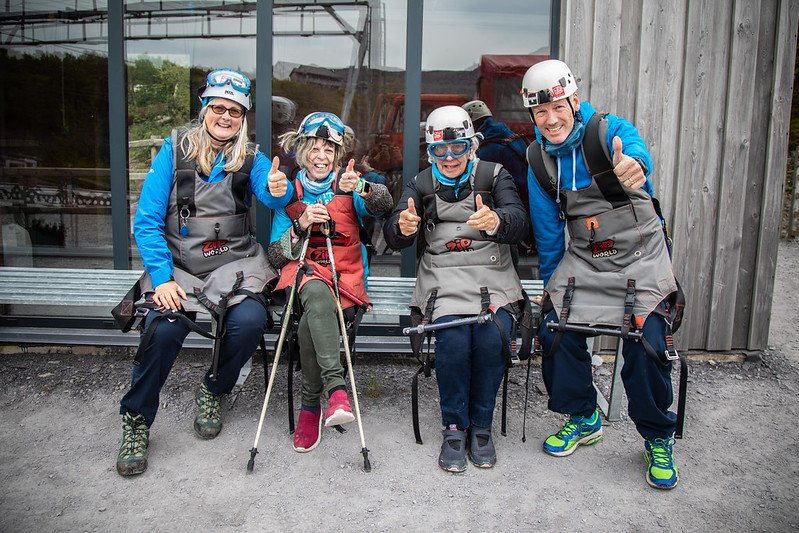 Four smiling people sitting outdoors in safety gear, giving thumbs up