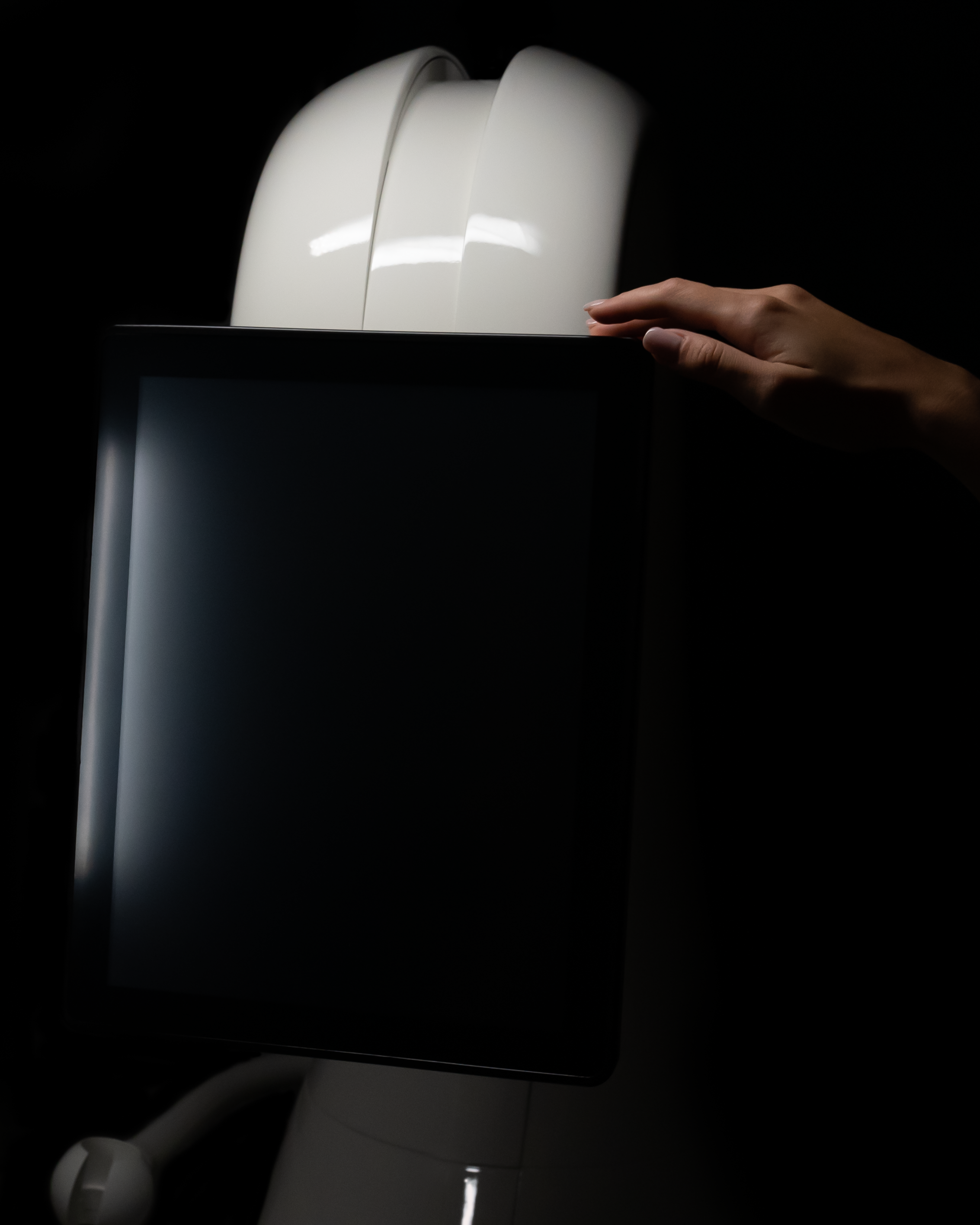 A person's hand adjusting a touchscreen monitor on a medical or diagnostic machine with a dark background.