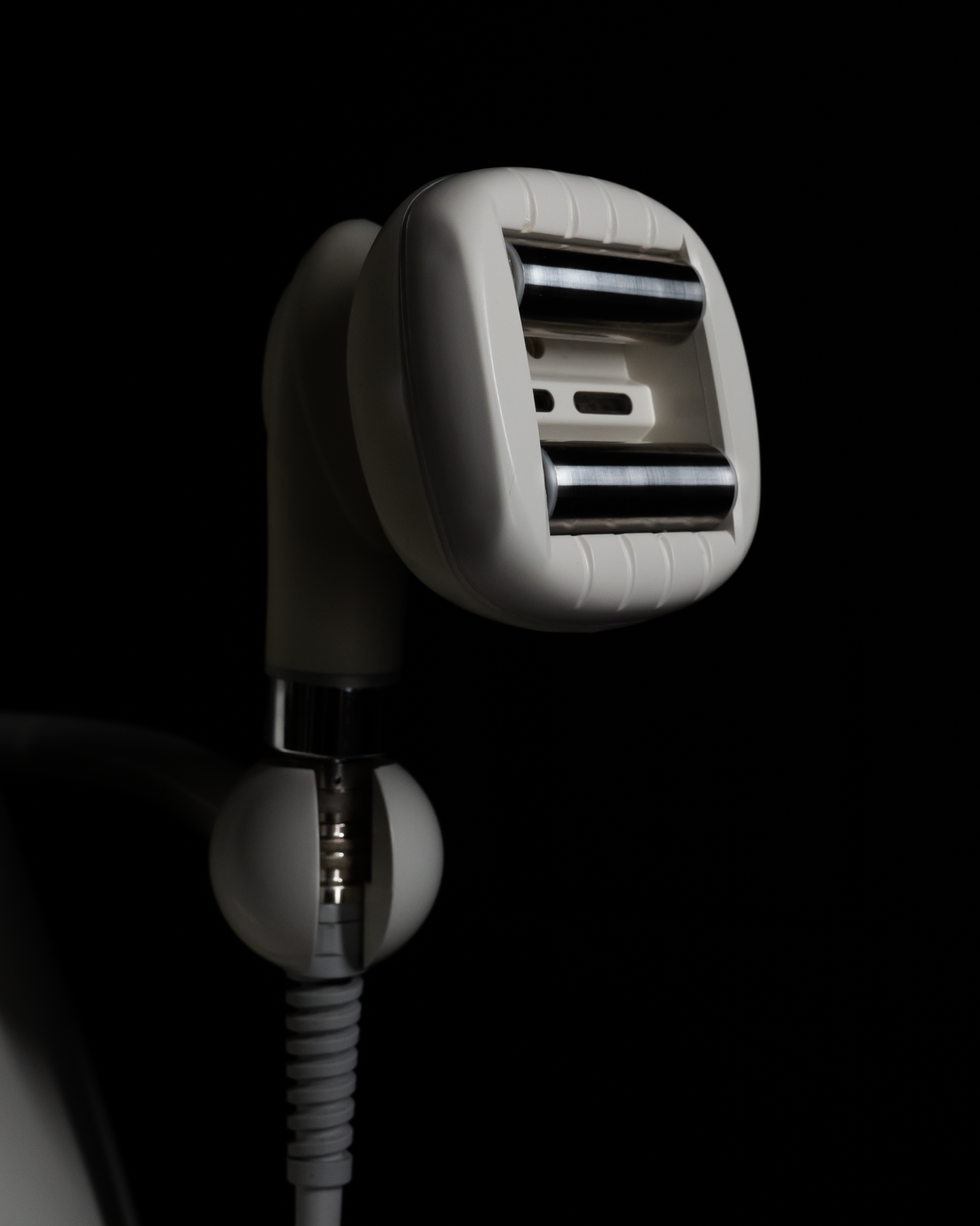 Close-up of a white, handheld, electric facial pore cleaner with two roller heads, against a black background.