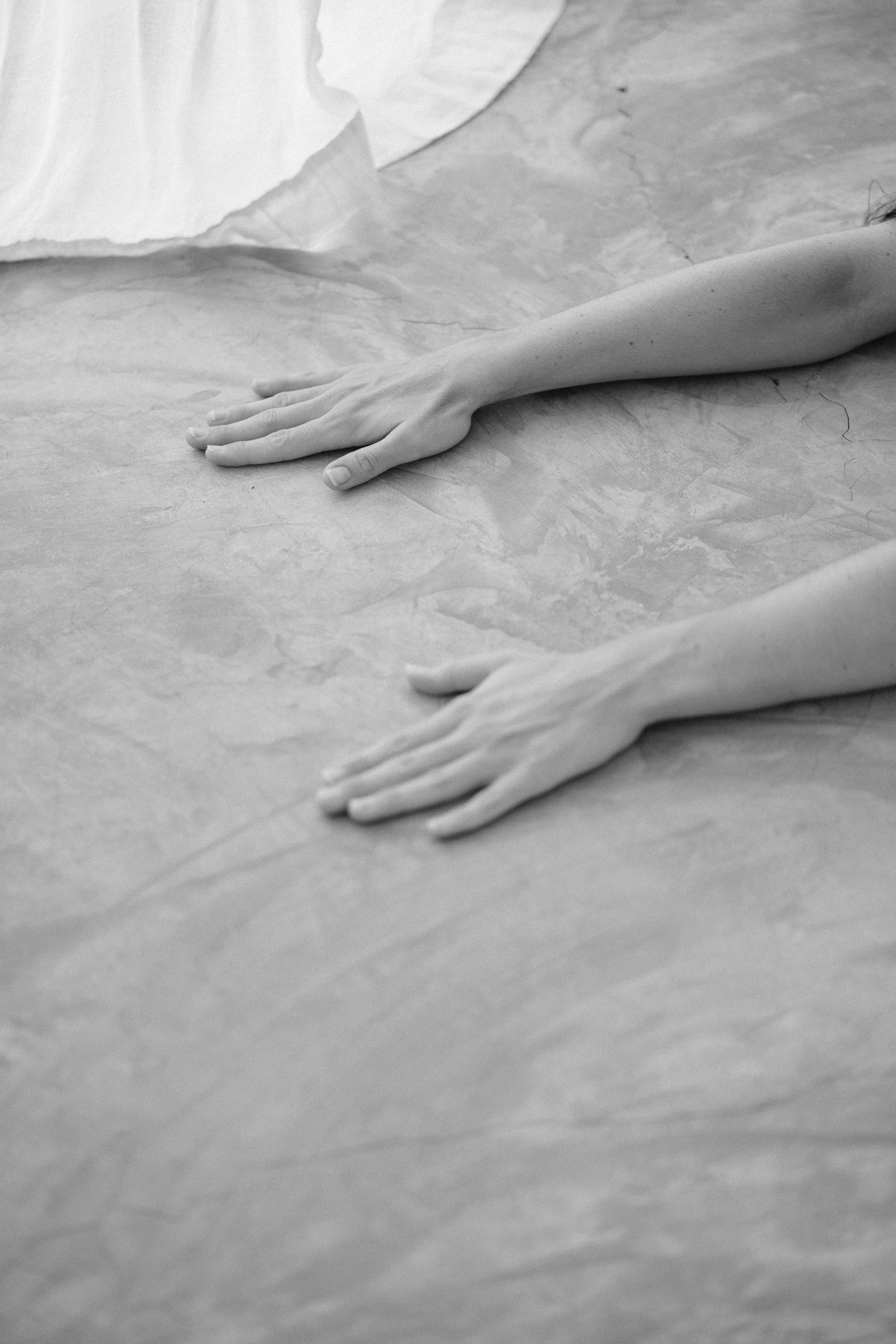 Close-up of a white human hand resting on a textured surface, possibly a table or floor, with the fingers extended and relaxed.
