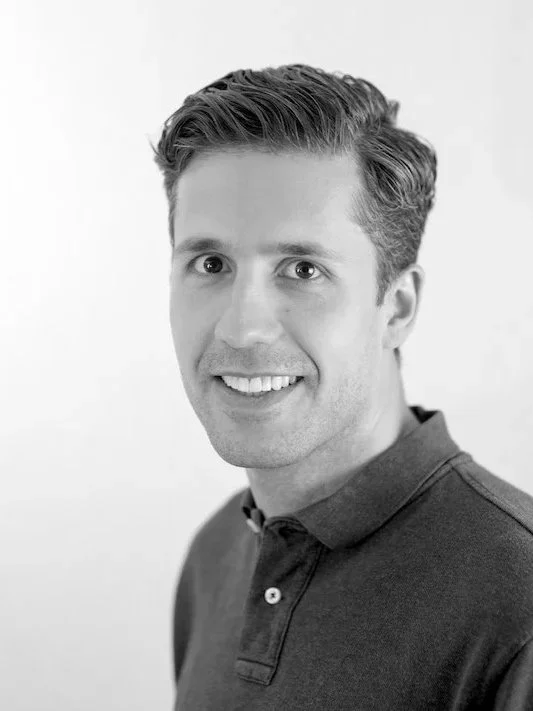 Black and white portrait of a smiling man, the owner of Luxe Smart Homes, Richard Colman with short hair wearing a dark polo shirt.