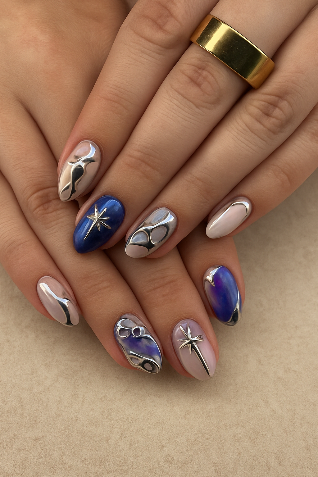 Close-up of manicured fingernails with metallic, blue, purple, and pearl designs, and a gold ring.