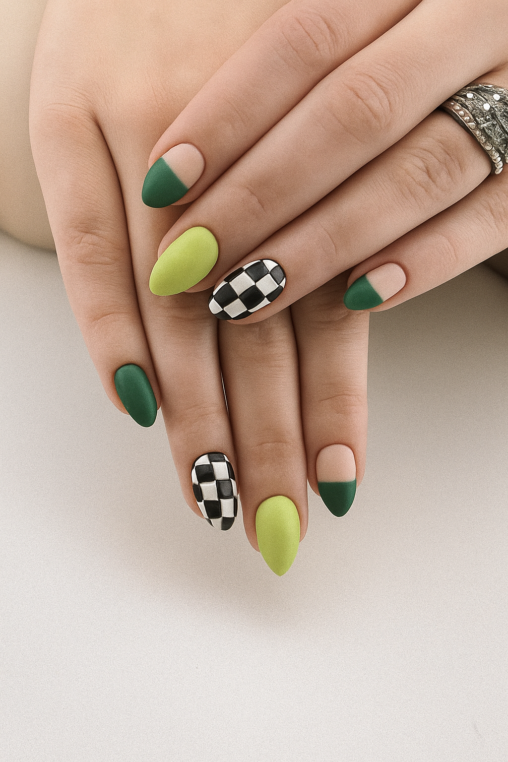 Close-up of hands with manicured nails in green, lime, and black-and-white checkered designs, and rings on fingers.
