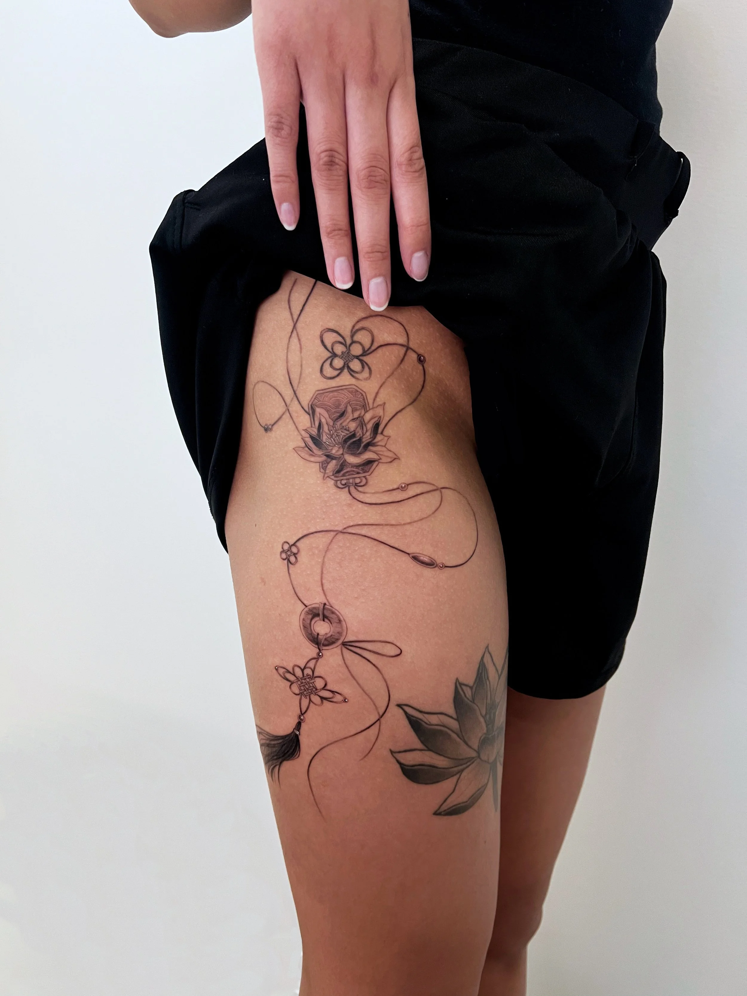 Tattoo of a lotus flower charm on a person's thigh, with a dreamcatcher design.
