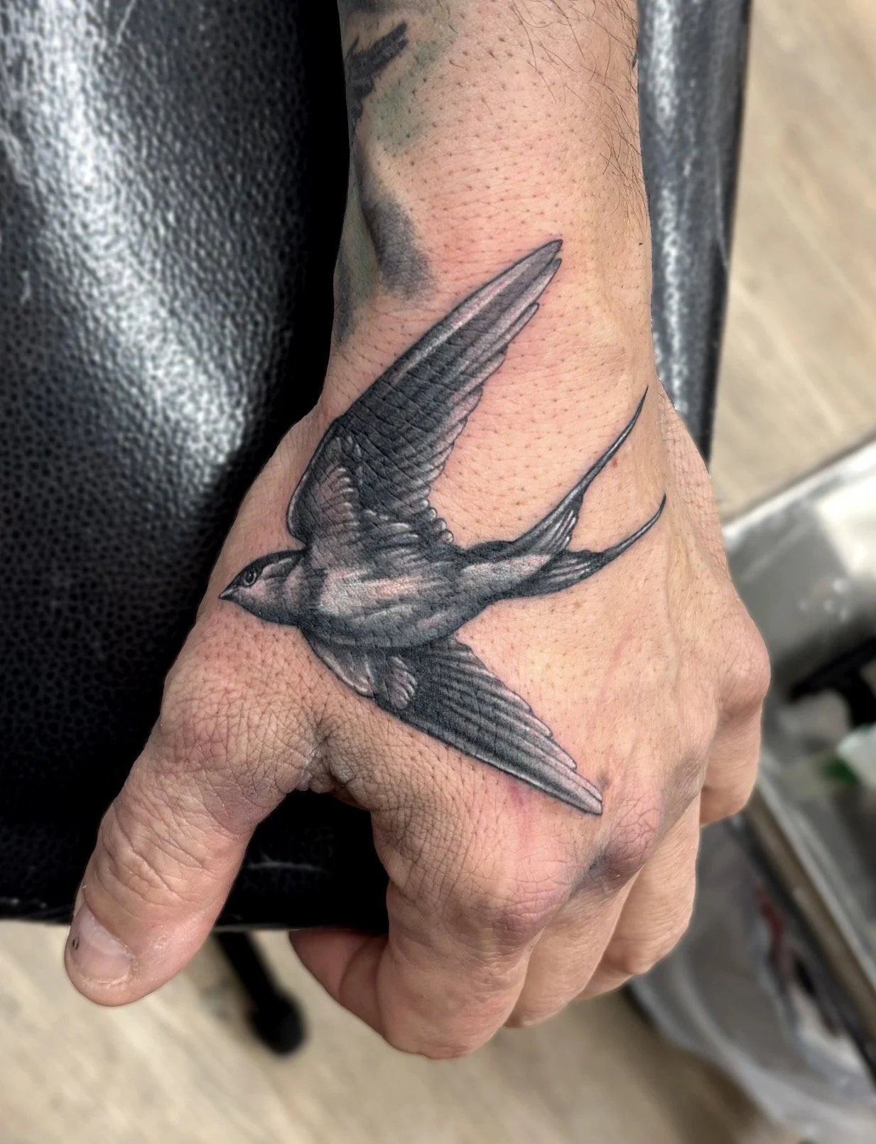 Black and grey realism tattoo of a flyin swallow on a person's hand.