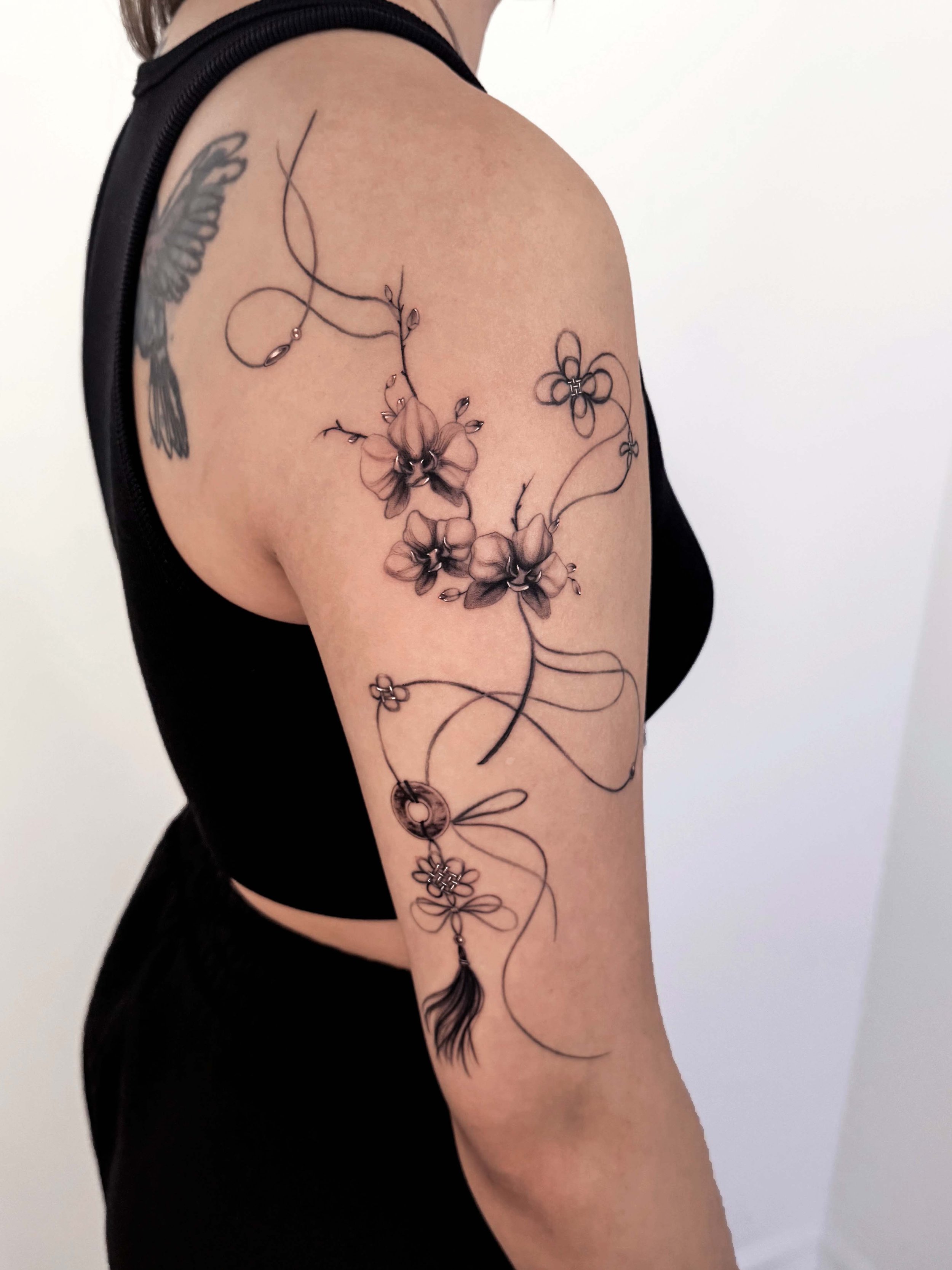 Tattoo of flowers and a dreamcatcher on a person's upper arm and shoulder.