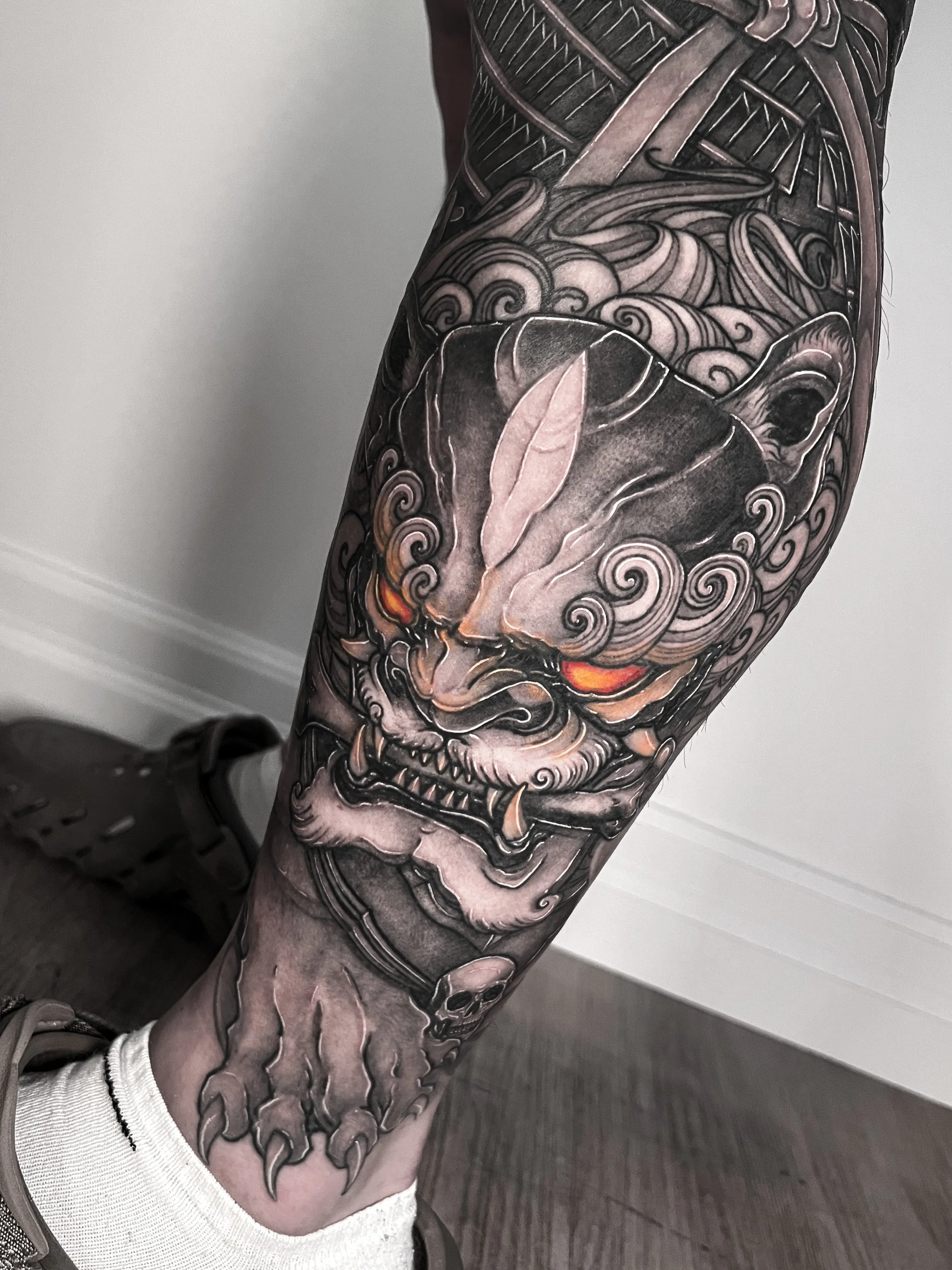 Black and grey Japanese/Asian tattoo of a fierce Foo Dog with glowing orange eyes on a person's calf.