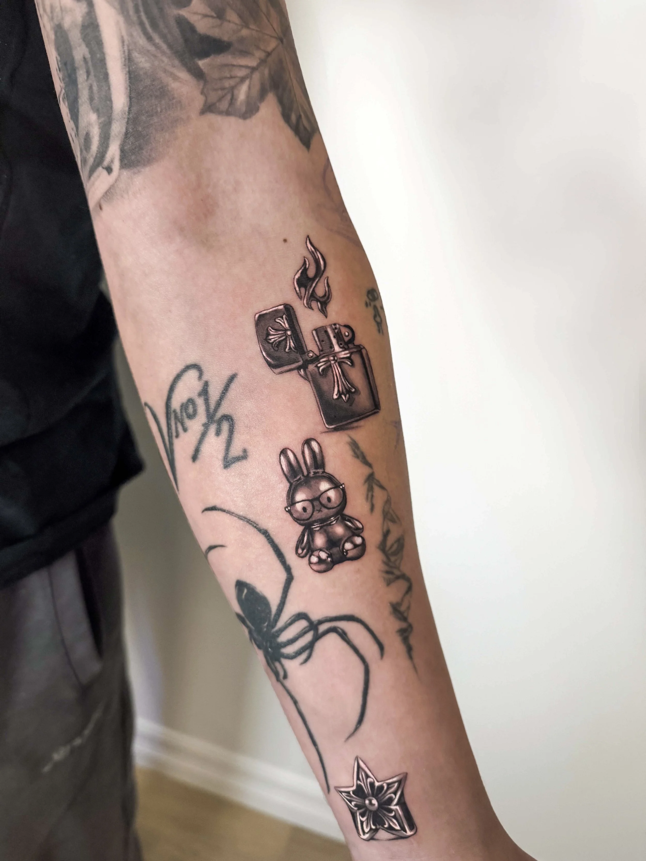 Tattoo sleeve with a chrome style effect chrome hearts silver lighter with flames, a cartoon bunny Miffy Sanrio character with glasses, a star, and a floral pattern.