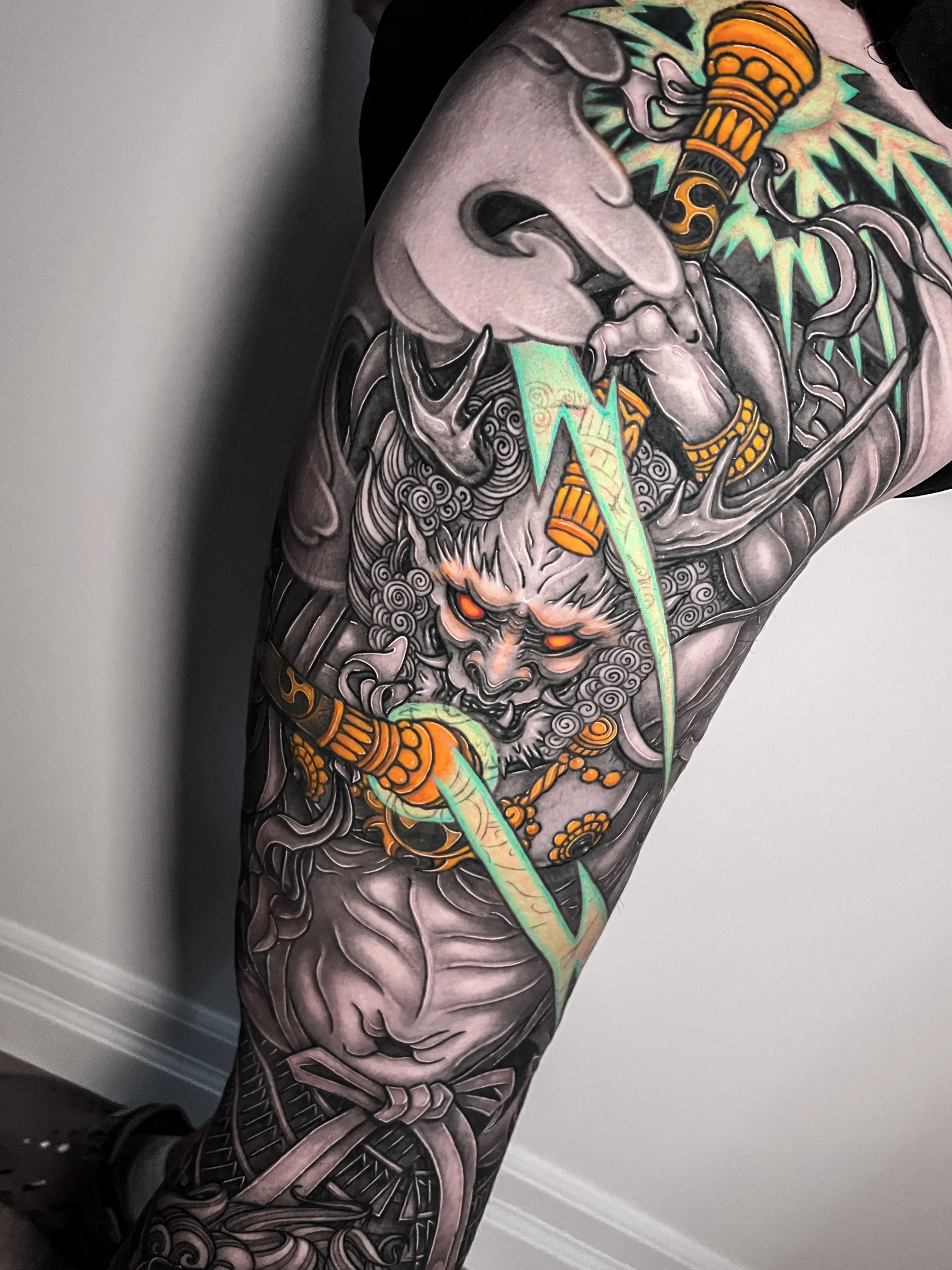 Japanese/Asian leg sleeve featuring the Japanese God of Thunder Raijin with glowing red eyes and blue lightning in a neo-traditional asian style.