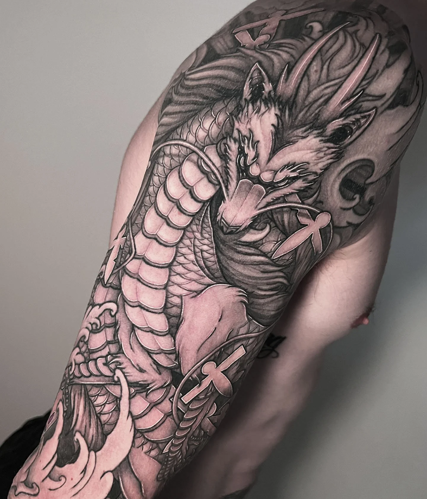 Black and grey tattoo of Haku from the movie "Spirited Away" in his dragon form on a person's upper arm and shoulder as a half-sleeve tattoo.