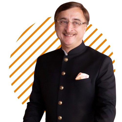 Man in a black traditional Indian suit with gold buttons and a white pocket square, smiling,