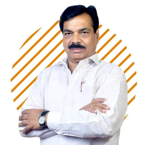 A man with dark hair and a mustache, wearing a white shirt with rolled-up sleeves, standing with arms crossed in front of a white background with orange diagonal stripes.