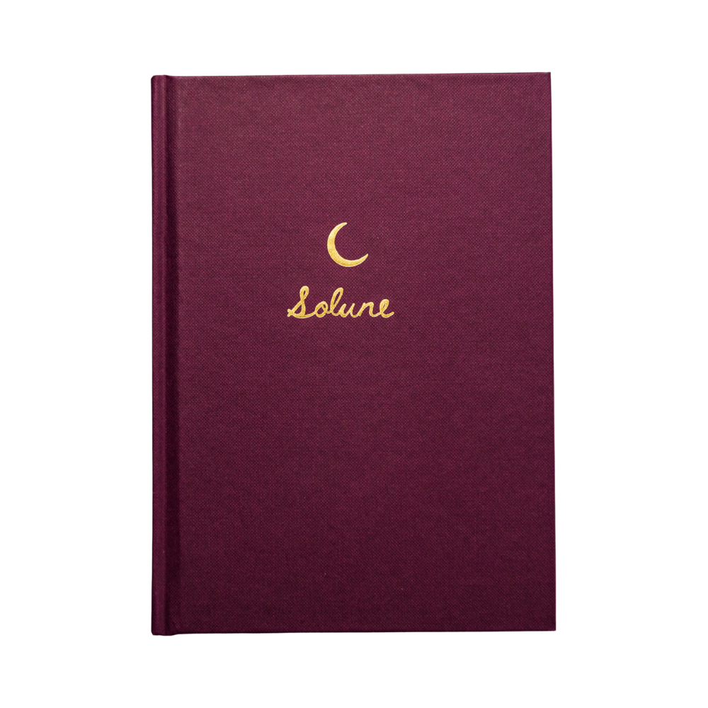 A burgundy hardcover journal with a gold crescent moon symbol and the word 'Solune' written in gold on the cover.
