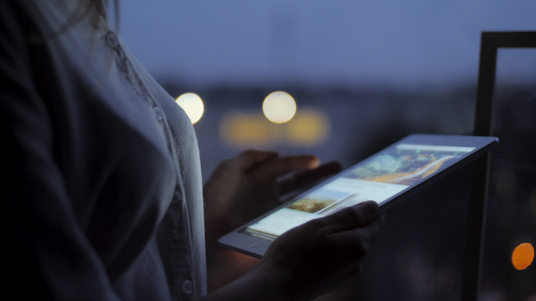 Person using a tablet outdoors during evening or night, with blurred city lights in the background.