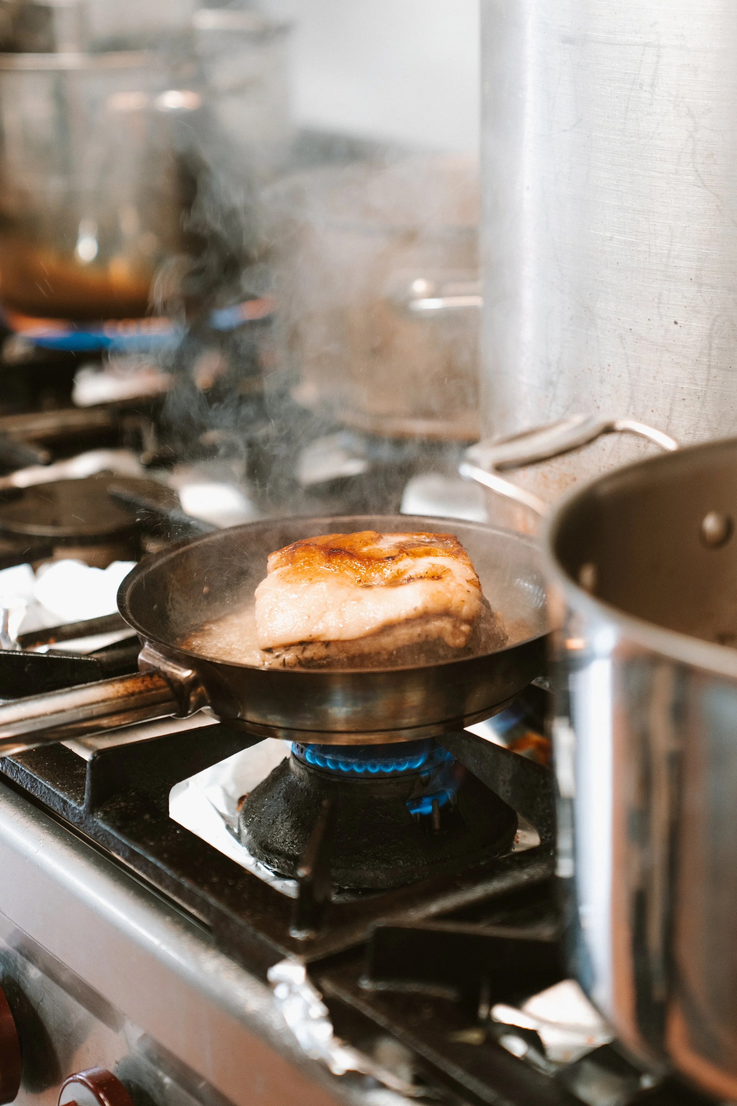 Vis bakt in een pan op een kookplaat, met stoom die opstijgt.