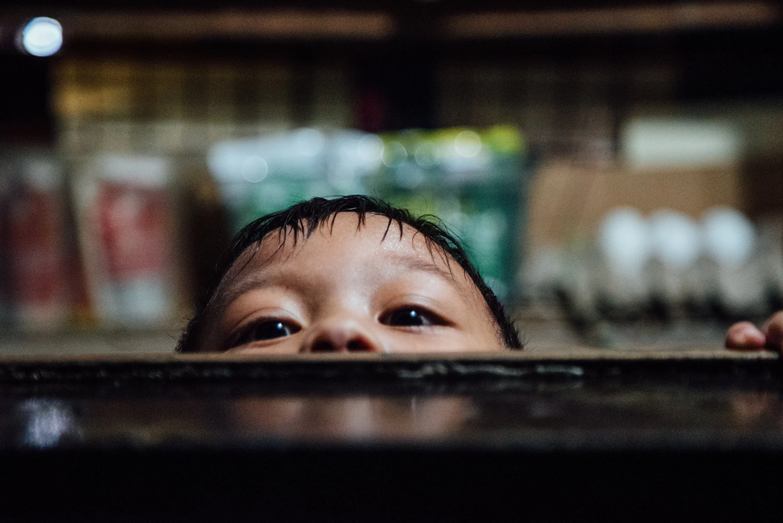 A young child peeking above a black surface, with a blurred background.