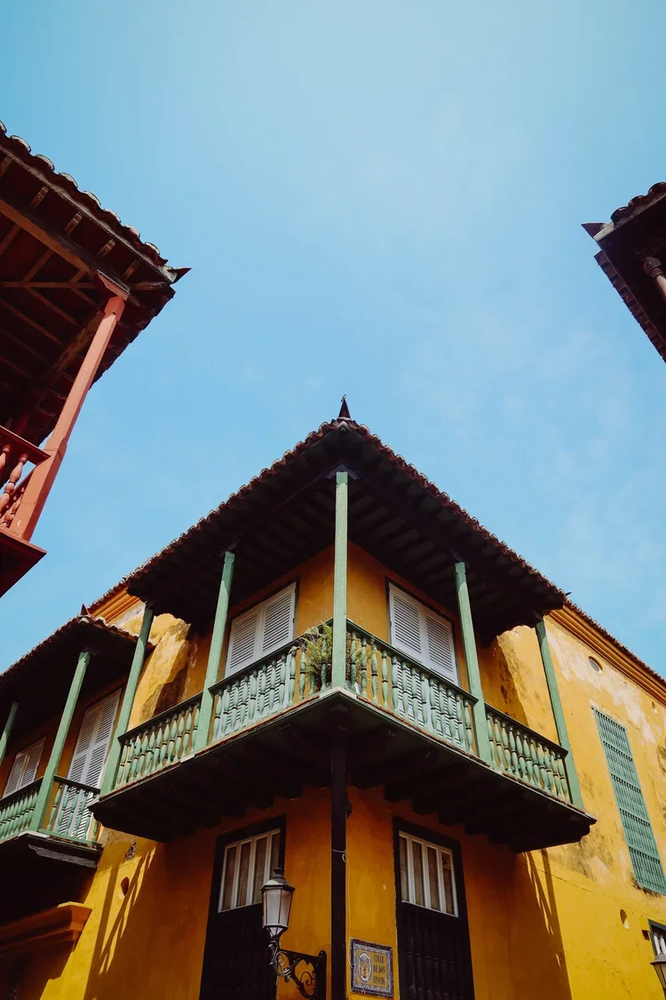 A colorful yellow building with green balconies and shutters, set against a clear blue sky.