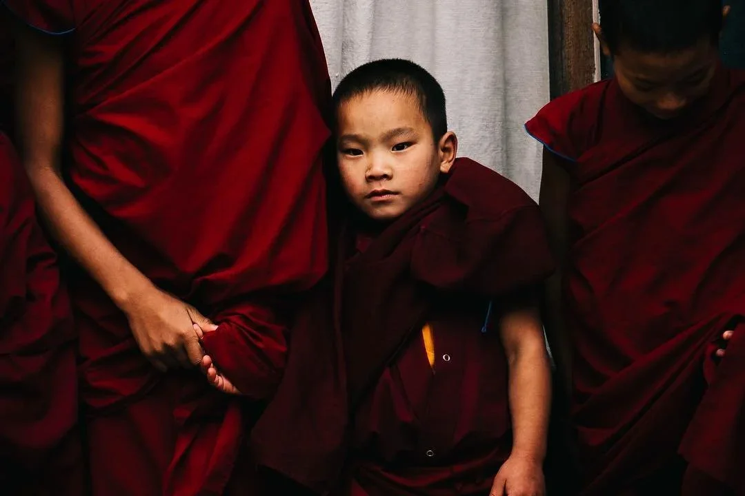 A young boy in maroon robes standing between two monks, one holding his hand.