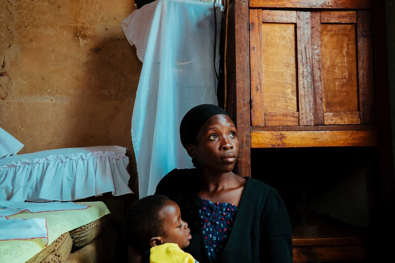 A woman with a child indoors, a wooden wardrobe in the background.