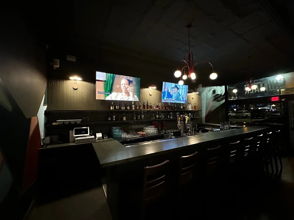 Bar at night with two TVs above a counter lined with bottles