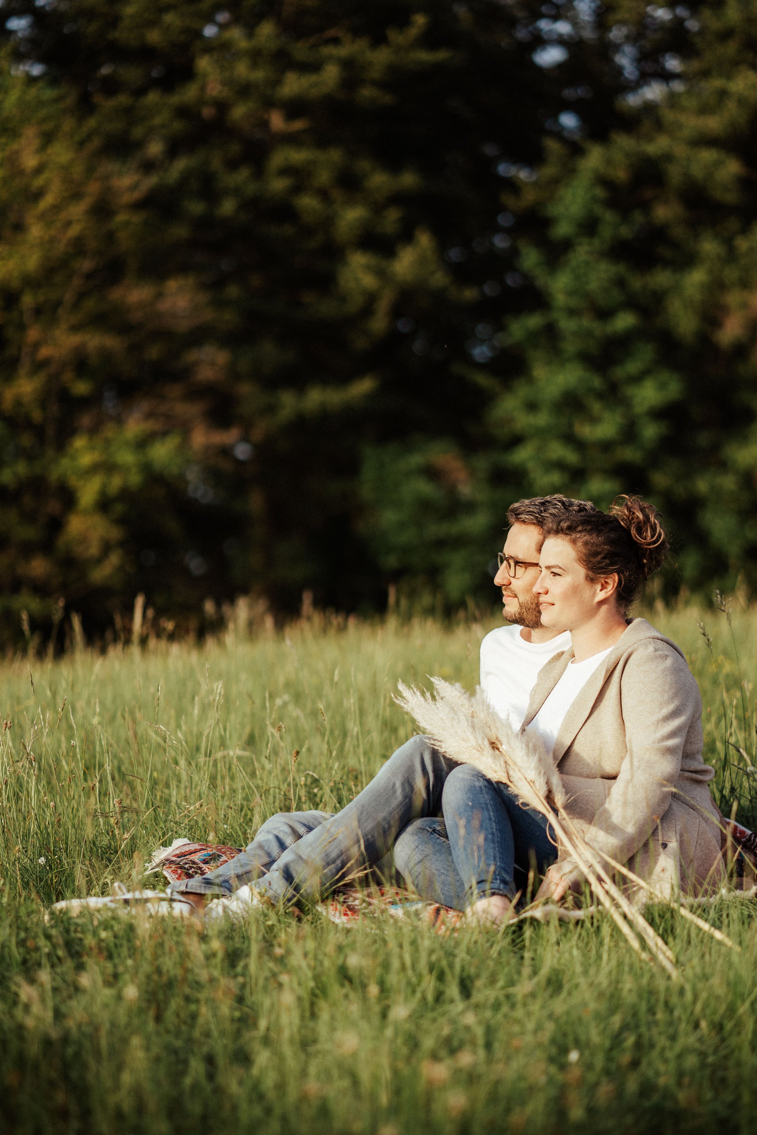 Paarshooting in der Abendsonne: Paar in Jeans und weißem T-Shirt sitzt auf Wiese  mit Blick in die Sonne by UhlArt Fotografie