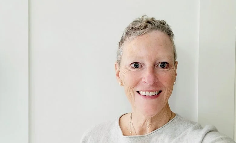 Smiling person with short hair wearing a light-colored shirt against a plain background.