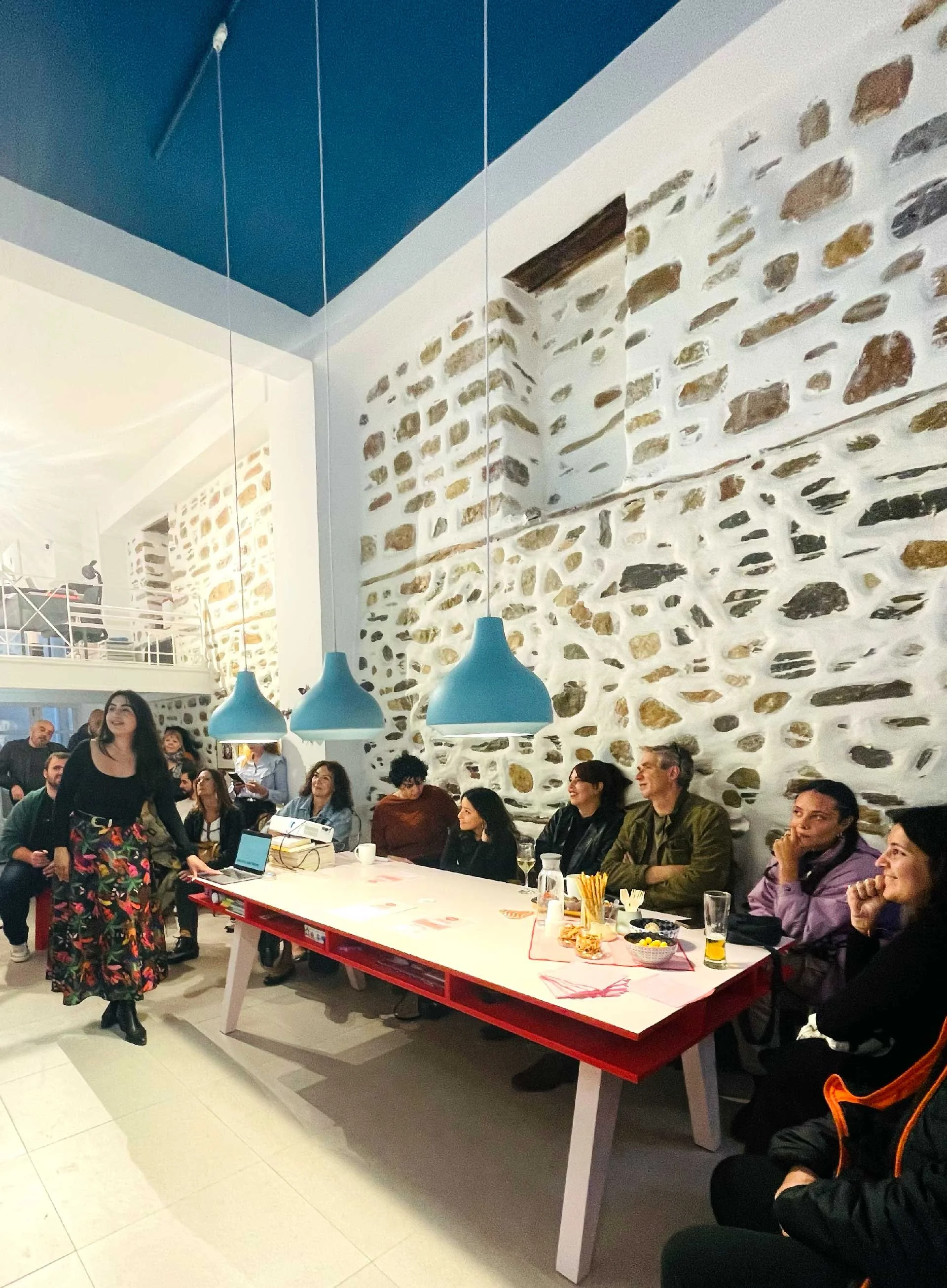 Creative Exchange community event at Until Sunday Studio in Syros, featuring a group of creatives gathered around the studio space while a guest speaker presents their work.