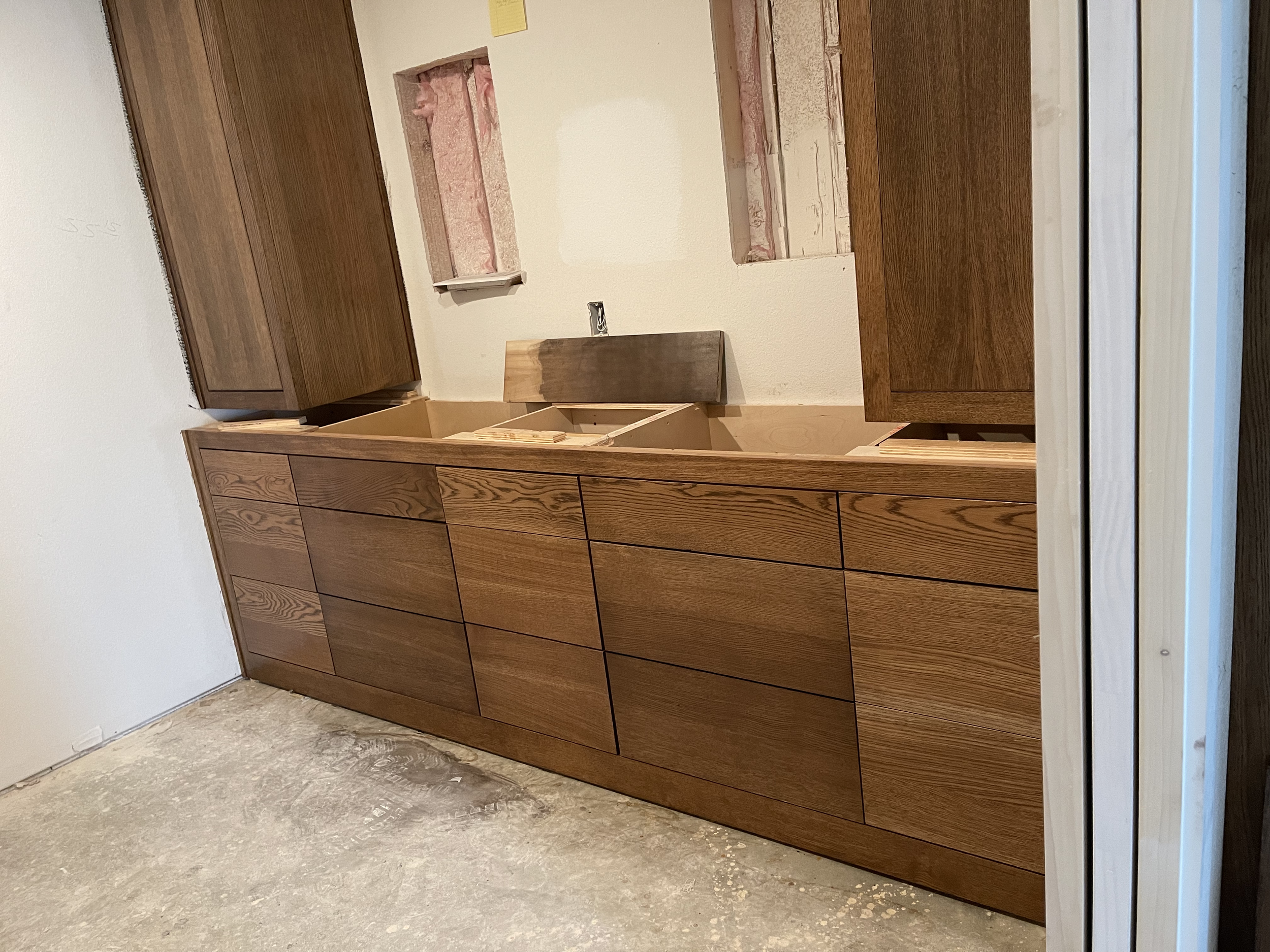 Kitchen cabinet installation in progress with wooden cabinets and unfinished wall openings.