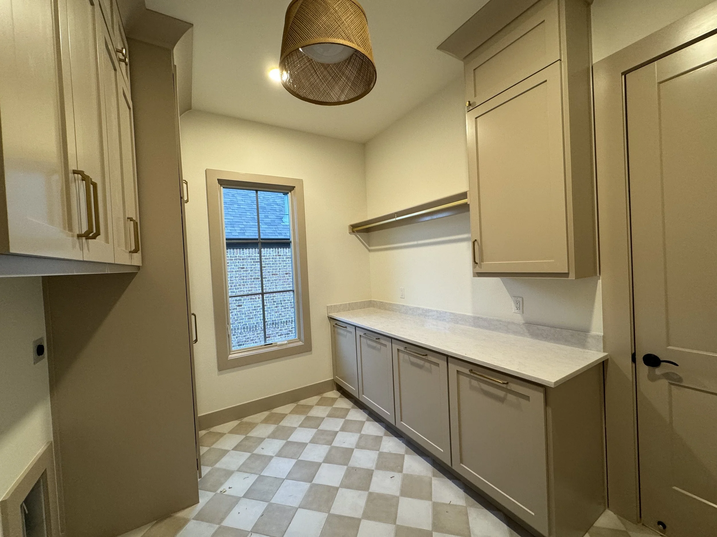 Empty laundry or utility room with beige cabinets, a window, and checkerboard tile flooring.
