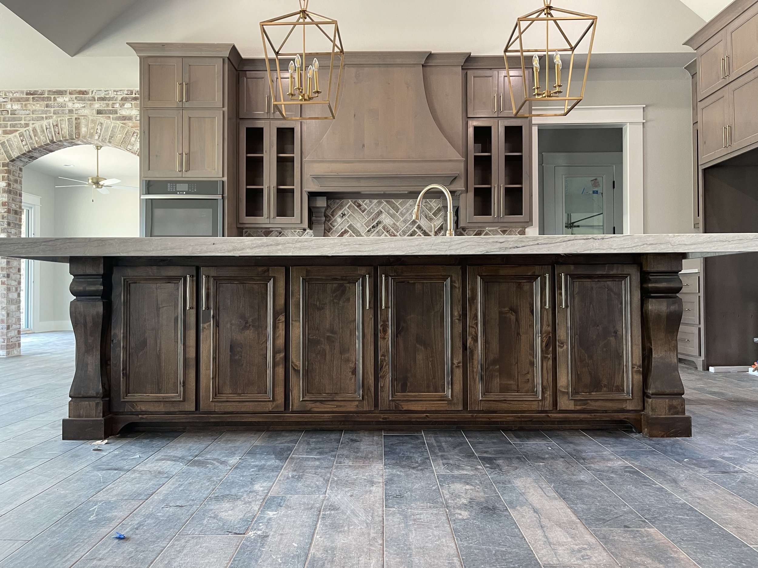 Modern kitchen with dark wood island, gray cabinetry, brick backsplash, and high ceiling.