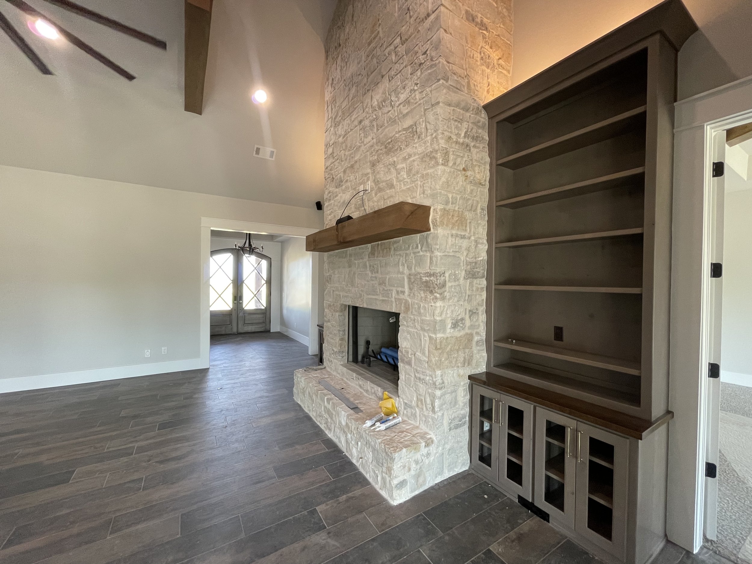 Interior of a room with a stone fireplace, wood mantel, built-in shelves, and dark wood flooring.