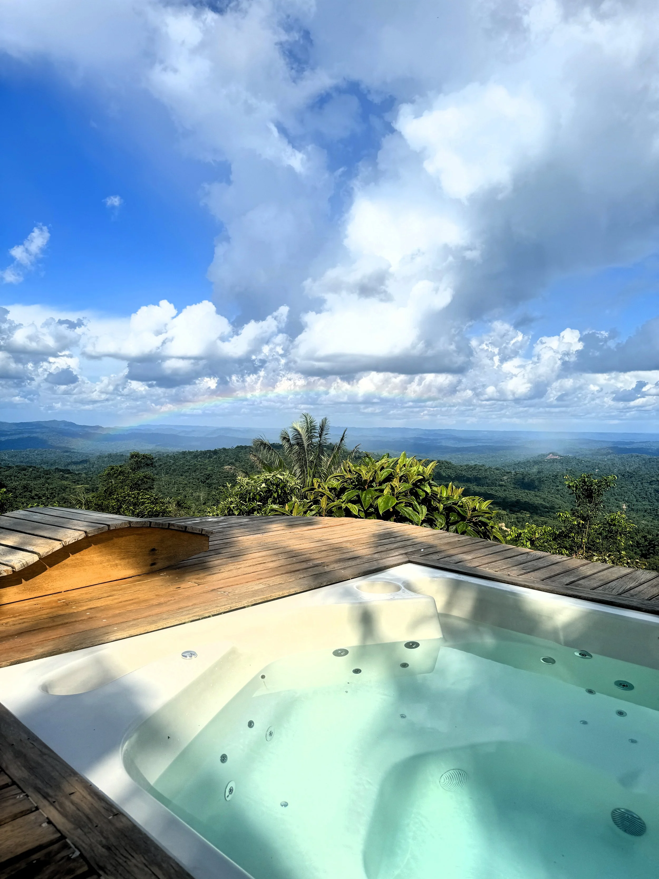 Jacuzzi en el mirador, con vista a un paisaje montañoso y un cielo con nubes y arcoíris.