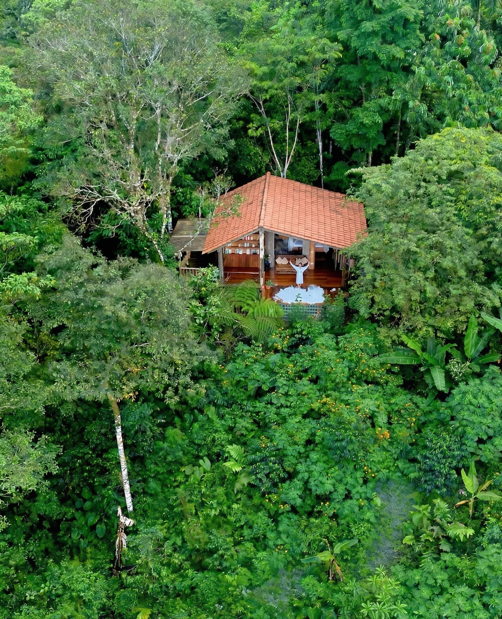 Suite Jaguar en medio de una selva tropical con techo de tejas rojas y una persona en la terraza levantando los brazos.