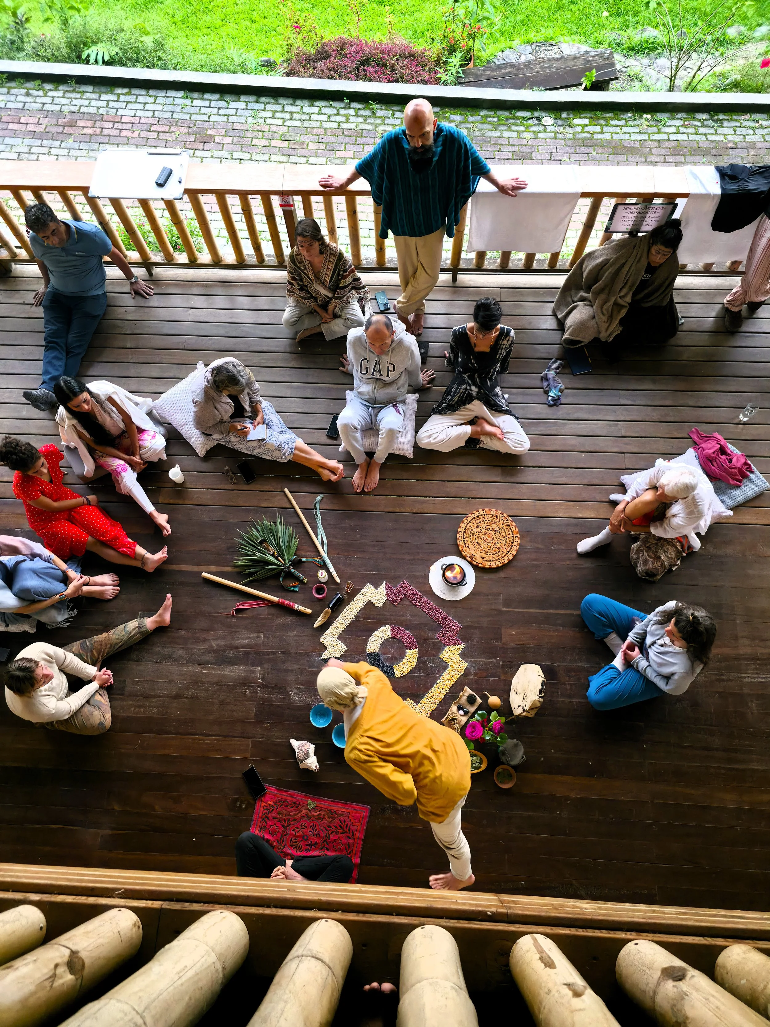 Grupo de personas participando en una ceremonia espiritual en un espacio cerrado con suelo de madera, con objetos rituales y decoraciones en el centro.