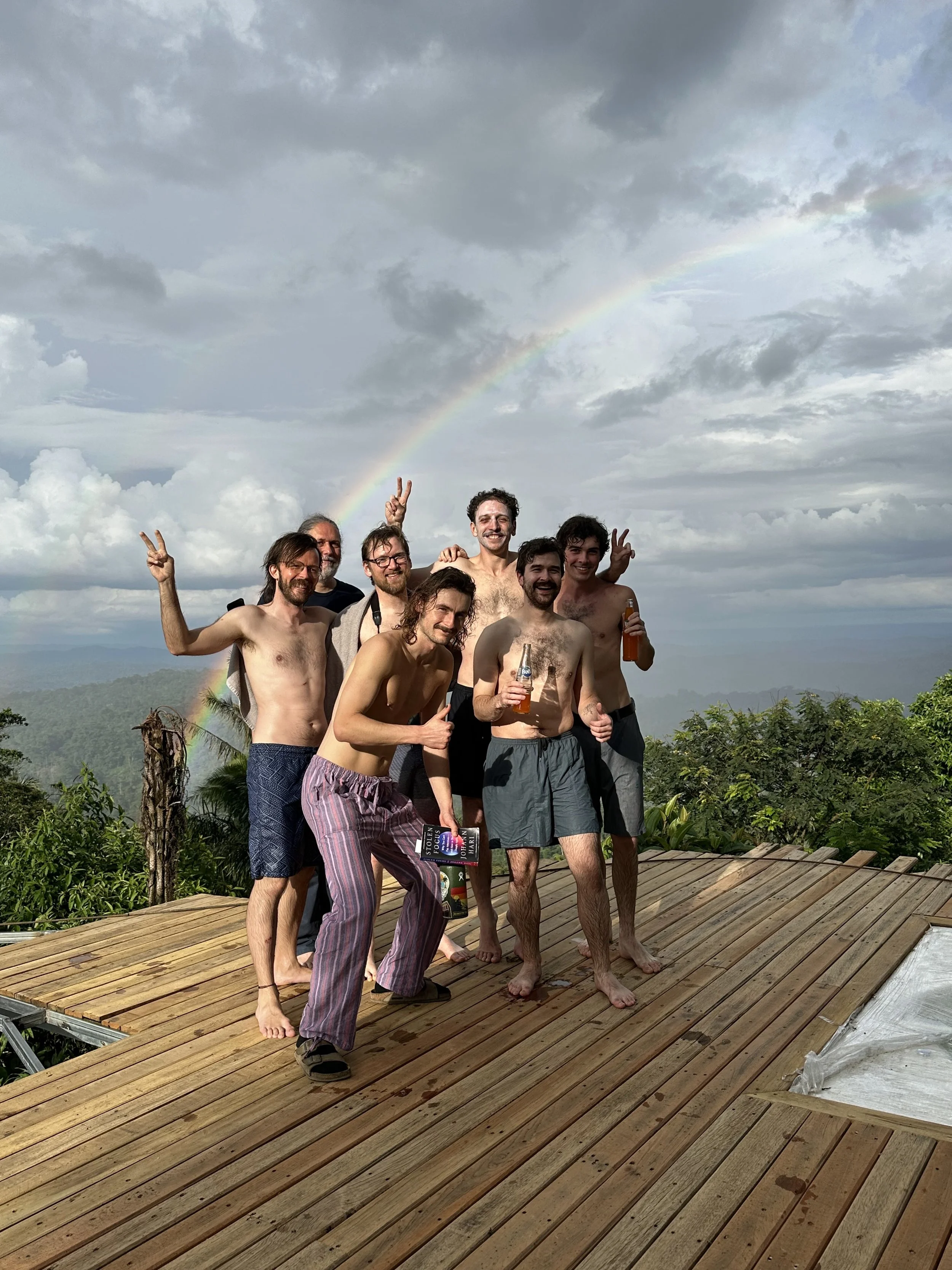 Grupo de siete amigos en el mirador, con un arcoíris y cielo nublado de fondo.